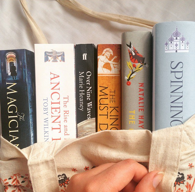 Tote bag with books coming out from the top - The Magicians by Lev Grossman, The Rise and Fall of Ancient Egypt by Toby Wilkinson, Over Nine Waves by Marie Heaney, The King Must Die by Mary Renault, The Children of Jocasta by Natalie Haynes, and Spinning Silver by Naomi Novik